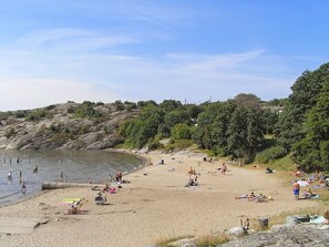 A beach with people sunbathing and swimming, surrounded by greenery and rocky terrain. - 4 Star Holiday Home in Lysekil (Lysekil)