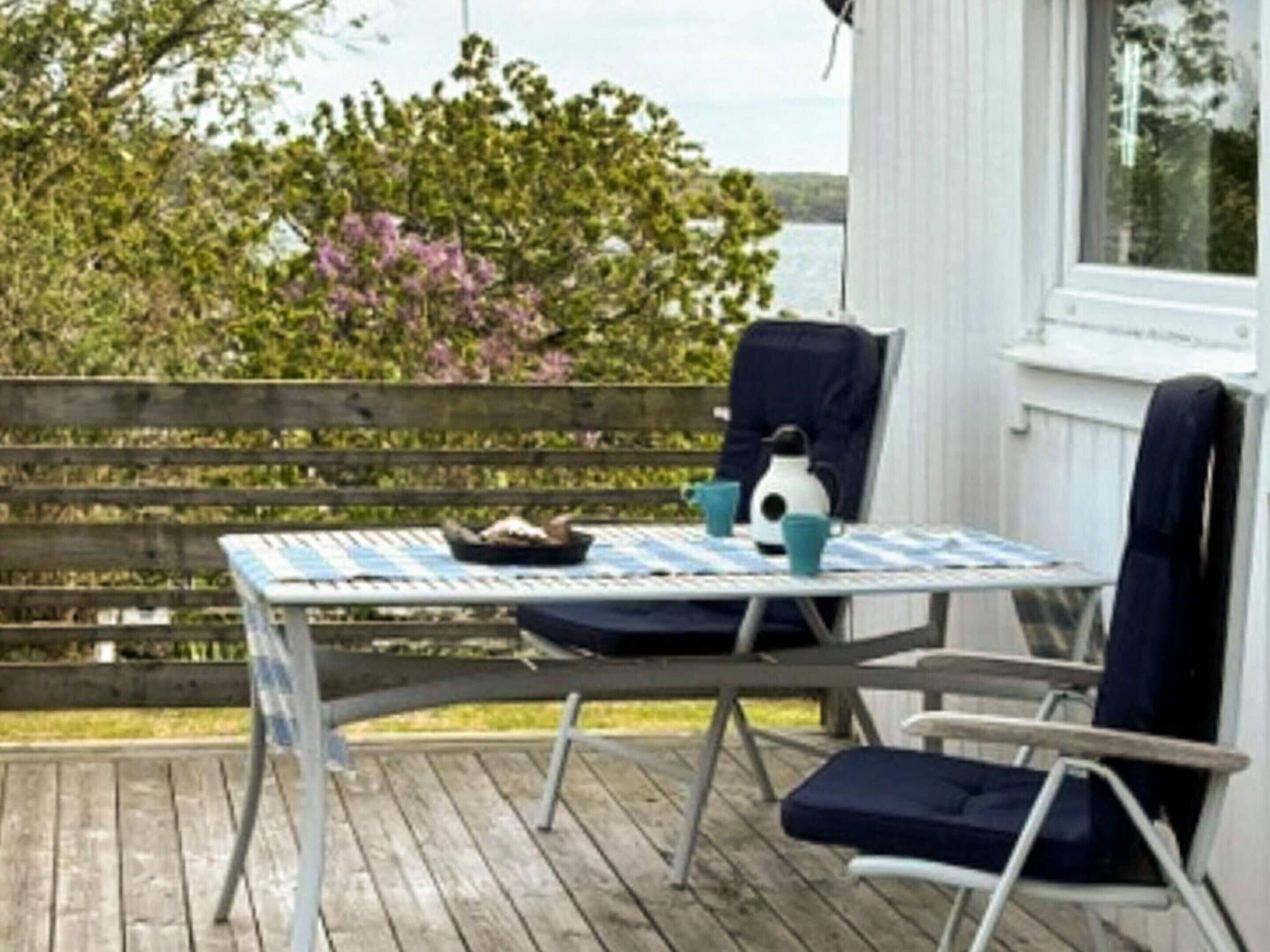 A wooden deck with a table and chairs, a bird feeder, and a view of the water.