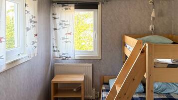 A room with a bunk bed, a small wooden shelf, a radiator, and a window with curtains.