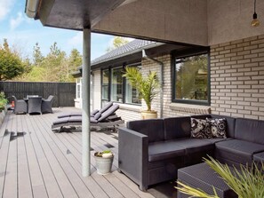 A covered outdoor patio with a dark-colored sofa, a dining table with chairs, and a potted plant. - 4 Star Holiday Home in Hemmet (Hemmet)