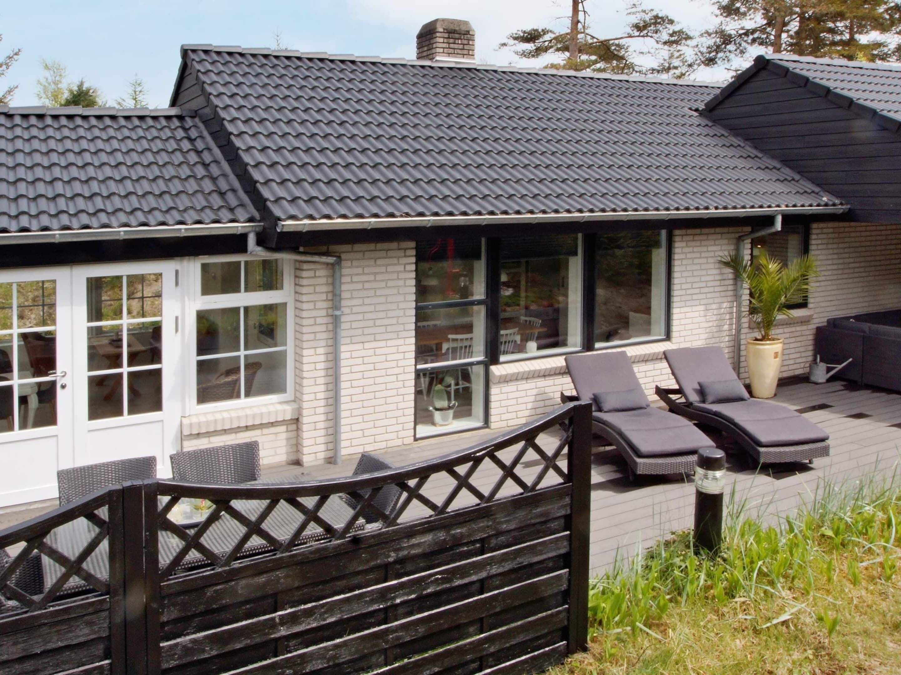 A modern house with a patio area featuring two lounge chairs and a wooden fence.