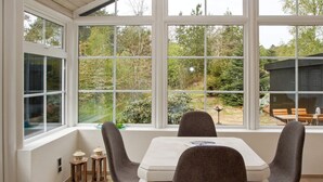 Ein Essbereich mit einem Tisch und vier Stühlen, große Fenster mit Blick auf einen Garten und Bäume.