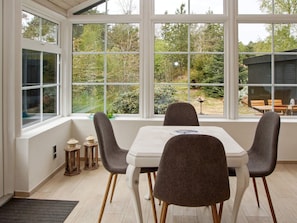 A dining area with a table and four chairs, large windows with a view of a garden and trees. - 4 Star Holiday Home in Hemmet (Hemmet)