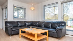 A modern living room with a black leather sectional sofa, a wooden coffee table, and large windows offering a view of the outdoors. - 6 Person Holiday Home in Ebeltoft (Ebeltoft)