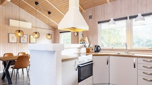 Una cocina moderna con vigas de madera, armarios blancos, una isla central e iluminación colgante.