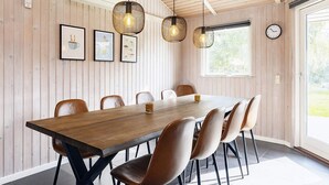 Un comedor con mesa y sillas de madera, lámparas colgantes, obras de arte enmarcadas y un reloj en la pared.