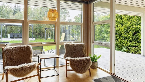 Una habitación con ventanas amplias, dos sillones mullidos, una mesa y una lámpara colgante.