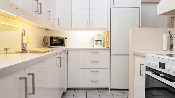 A modern kitchen with white cabinetry, a microwave, a coffee maker, and a stove. - 4 Star Holiday Home in Ebeltoft (Ebeltoft)