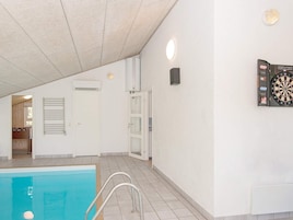 Una piscina con una escalera metálica, una puerta y un dardo en la pared.
