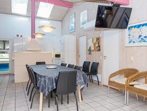 A dining area with a table, chairs, a television, and a wicker chair.