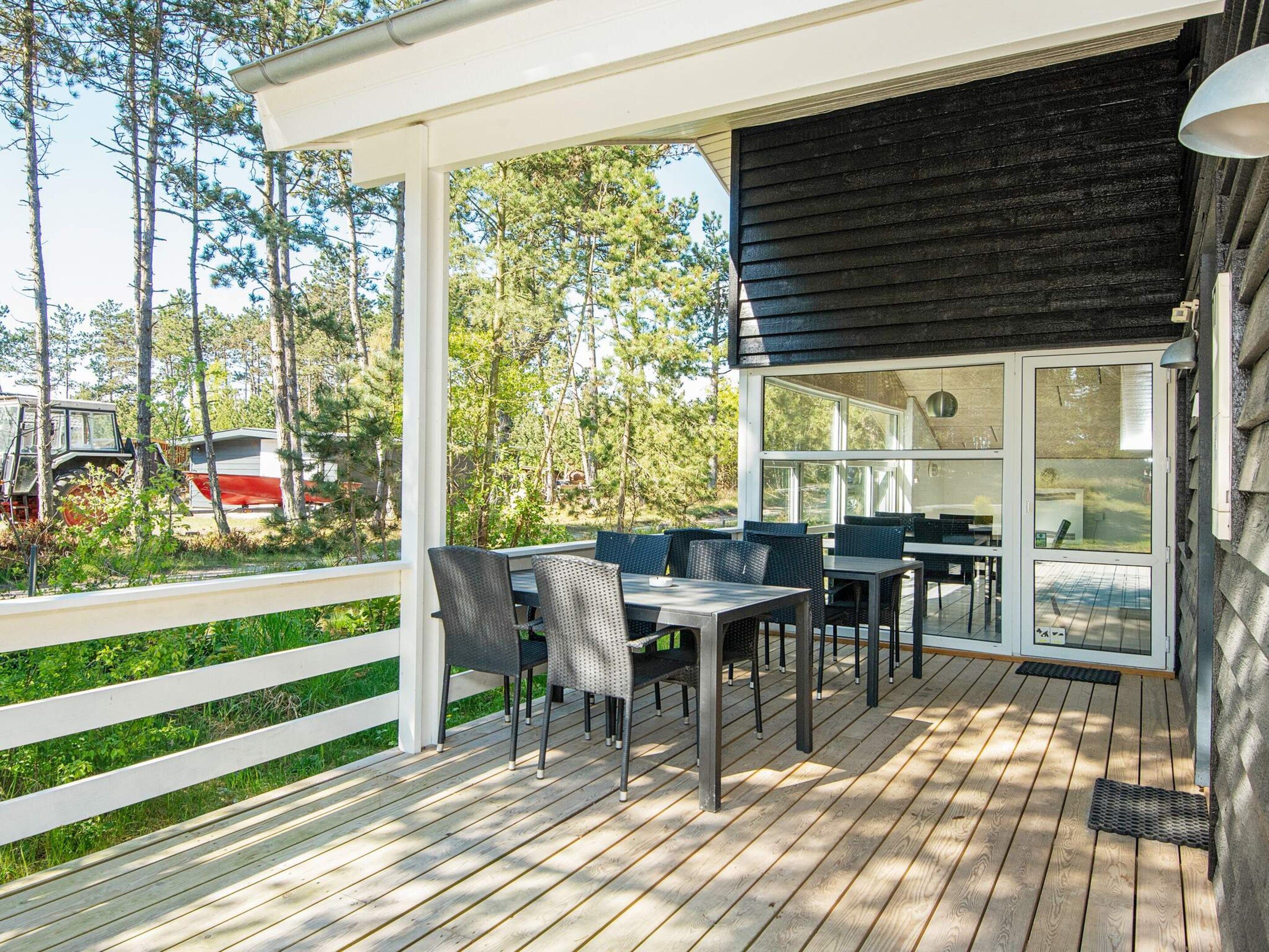 An outdoor deck with a dining area, surrounded by a white fence, and overlooking a forested area.