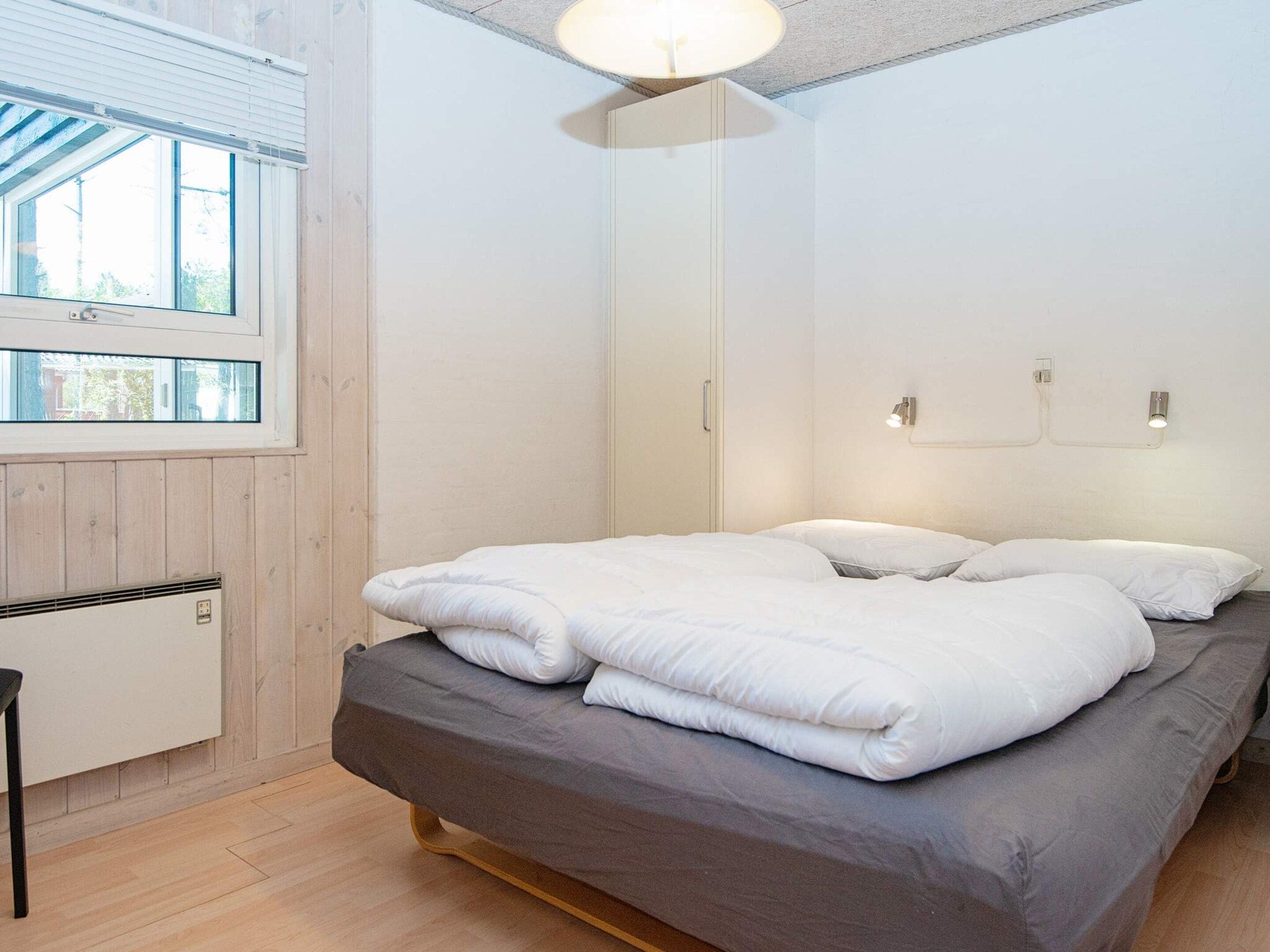 A bedroom with a bed, a window, and a wall-mounted light fixture.