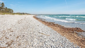 A pebble beach with waves, a clear sky, and a distant shoreline. - 4 Star Holiday Home in Ebeltoft (Ebeltoft)