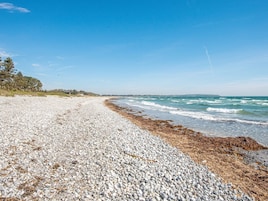 A pebble beach with waves, a clear sky, and a distant shoreline.