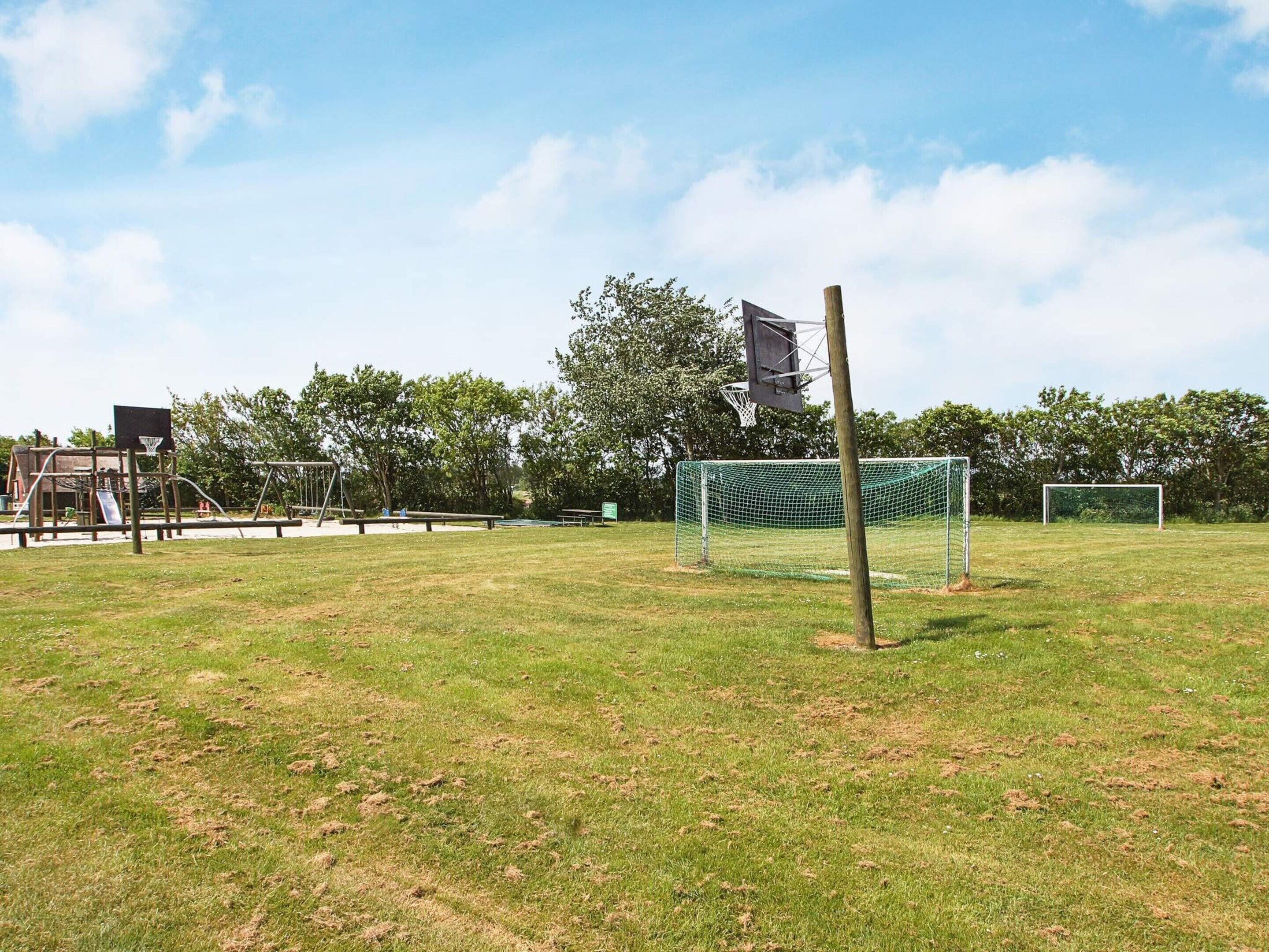A soccer field with a goalpost, a swing set, and a playground in the background.
