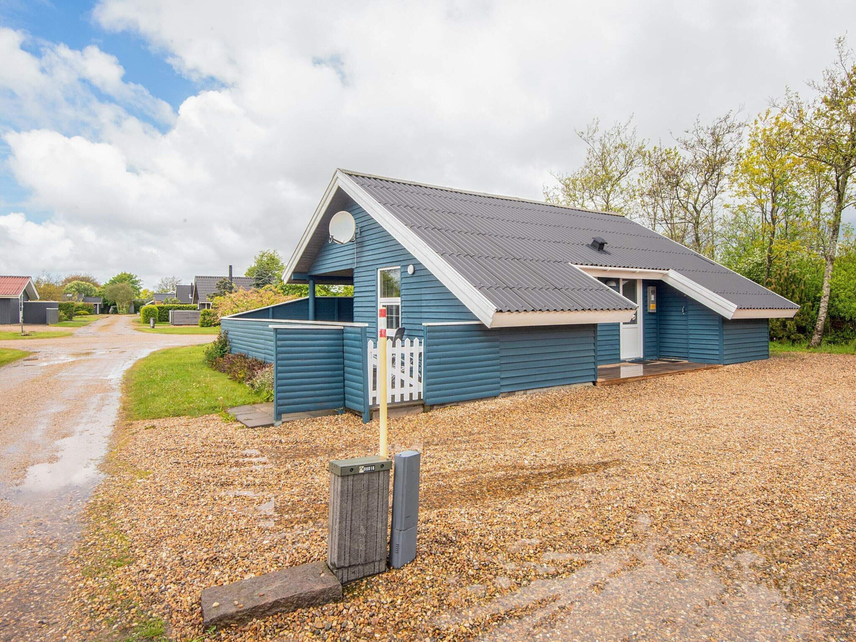 A blue building with a sloped roof, a gravel driveway, and a white picket fence.