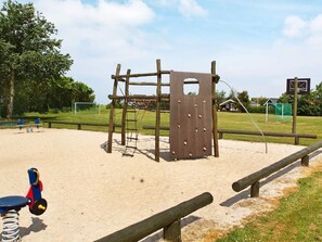 A playground with a wooden climbing structure, sand area, and a swing set.
