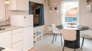 A compact kitchen with a refrigerator, a dining table with chairs, a window with curtains, and a small shelf with decorative items. - 4 Person Holiday Home in Hemmet (Hemmet)
