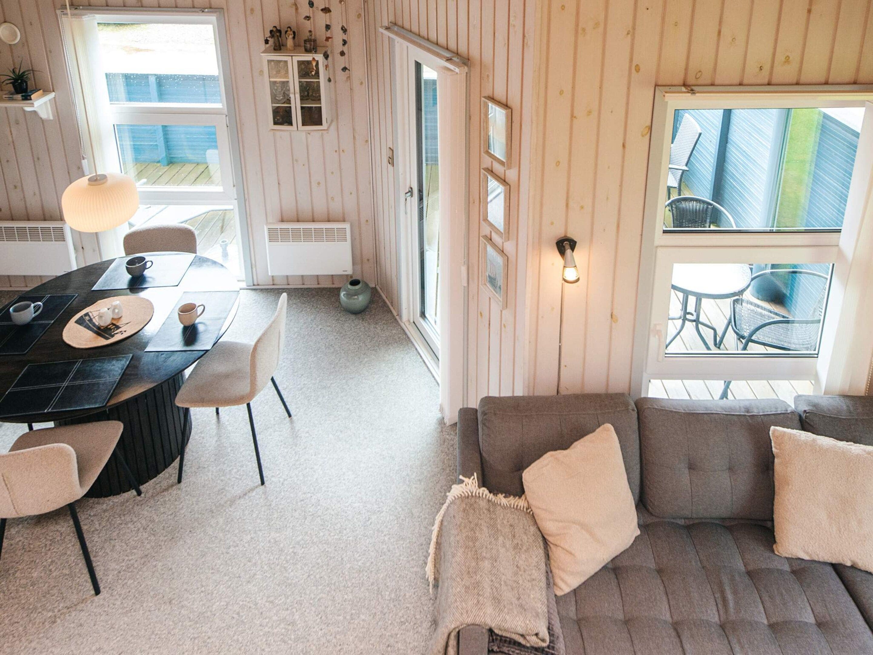 A cozy room with a dining table, chairs, a sofa, and a window overlooking a deck.