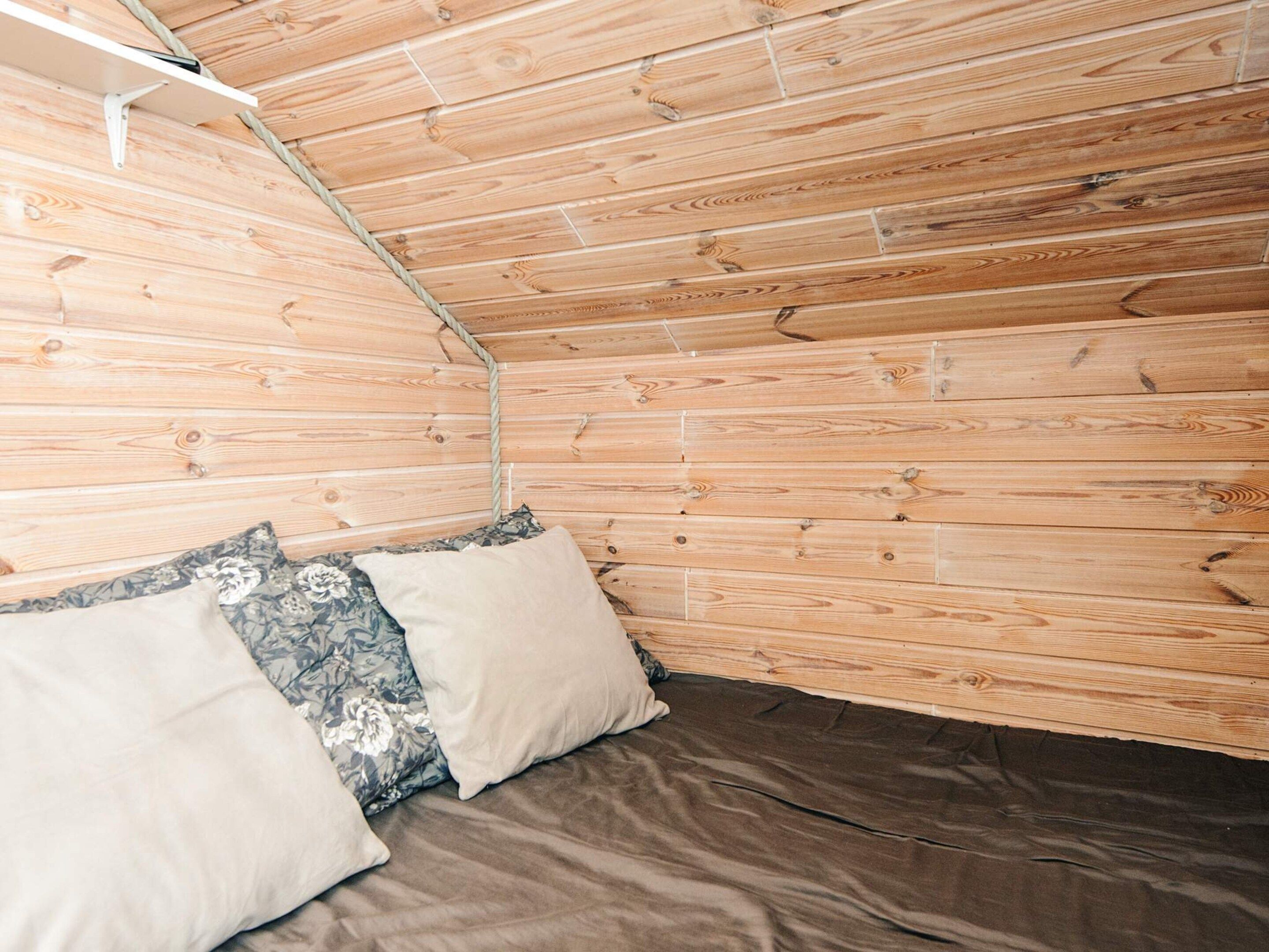 Una habitación con paredes de madera, una cama con colchón marrón y dos almohadas.
