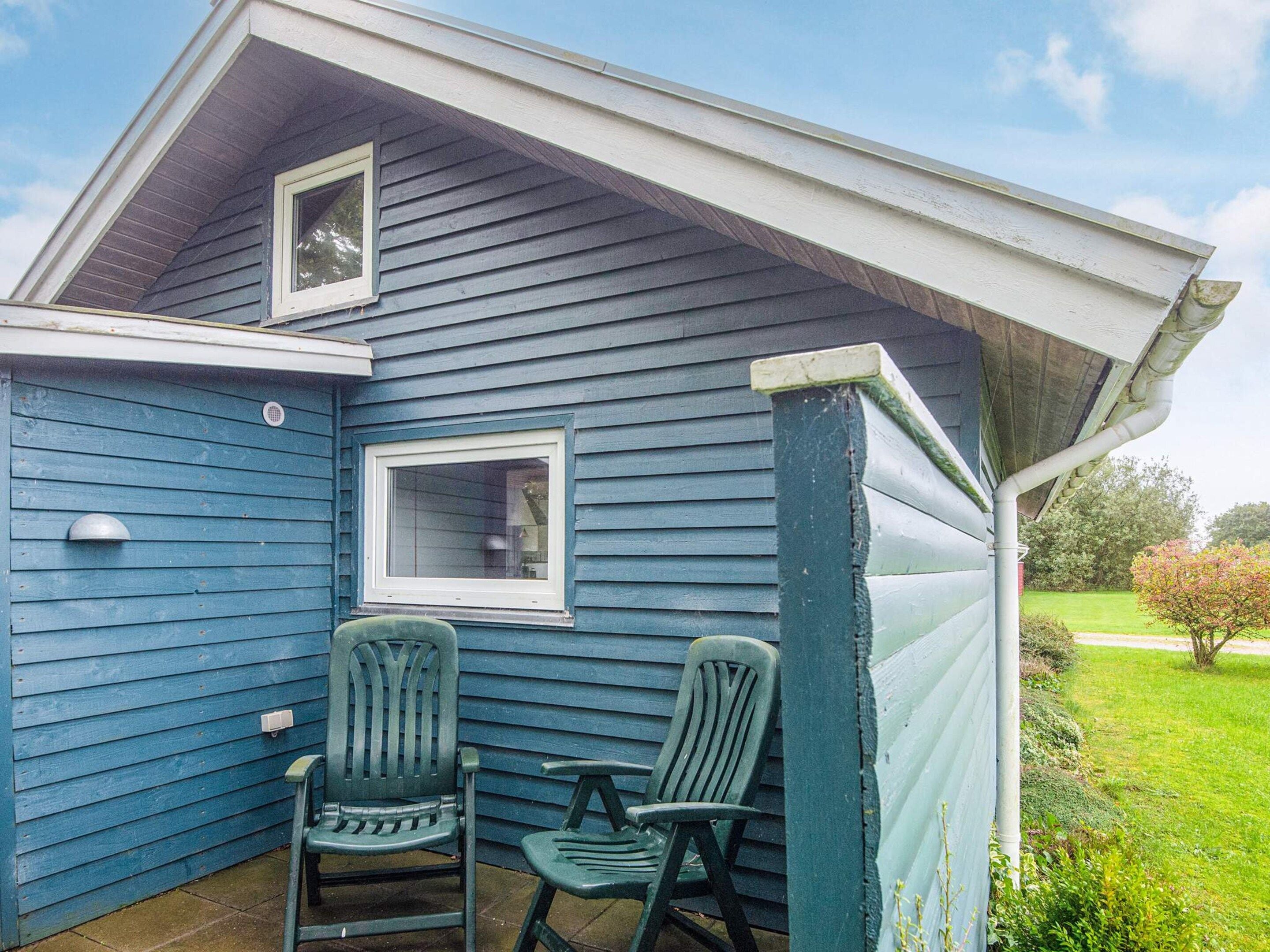 A blue house with two windows and a small porch with two chairs.