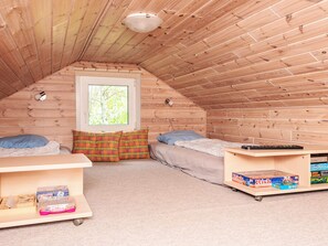 A small attic bedroom with two beds, a window, and a shelf with board games.