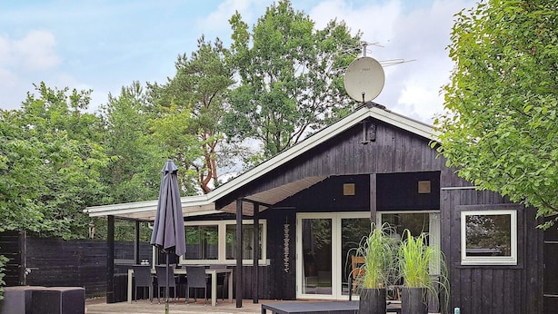 Une maison en bois avec un patio, du mobilier d’extérieur et une antenne parabolique.