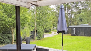 Une terrasse extérieure avec une table et des chaises, une plante en pot et un abri de jardin en arrière-plan.