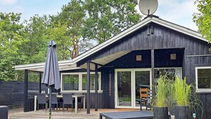 Une cabane moderne en bois, dotée d’une antenne parabolique, d’un espace extérieur aménagé et de plantes en pot.