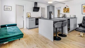A modern kitchen with a central island, bar stools, a green sofa, and a black chair.