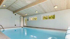 An indoor swimming pool with a wooden ceiling, windows, and a door.