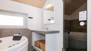 A modern bathroom with a large bathtub, a sink with a mirror, and a window above the sink.