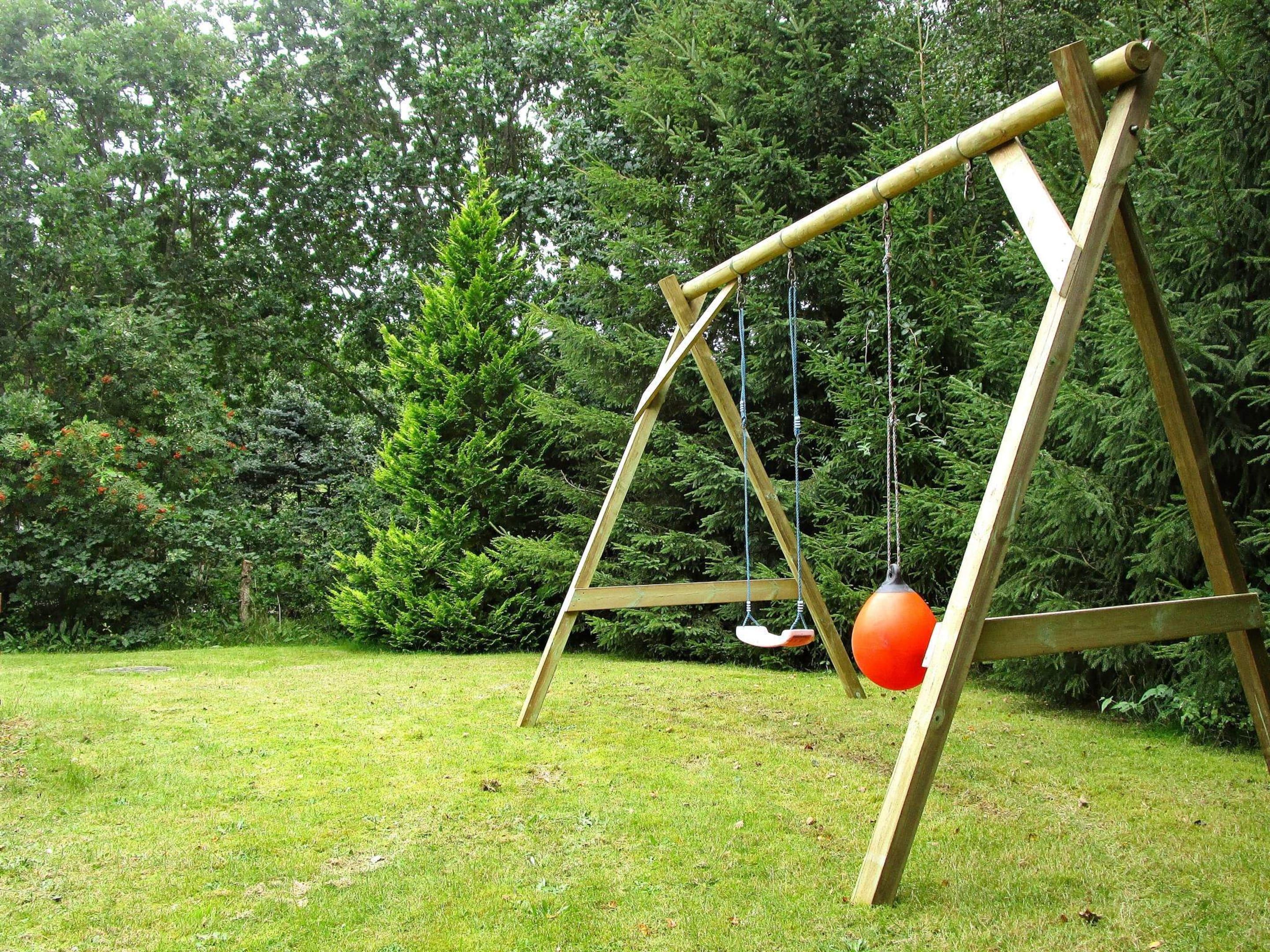 A wooden swing set in a grassy area with dense trees in the background.