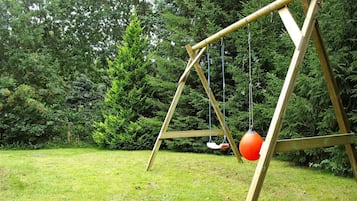 A wooden swing set in a grassy area with dense trees in the background.
