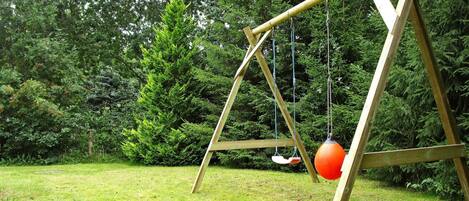A wooden swing set in a grassy area with dense trees in the background.