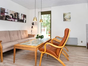 A living room with a sofa, a wooden dining table, a brown leather chair, and a hanging pendant light. - 6 Person Holiday Home in Glesborg (Glesborg)