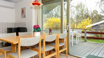 A dining area with a wooden table and chairs, a hanging light fixture, and a view of the outdoors.