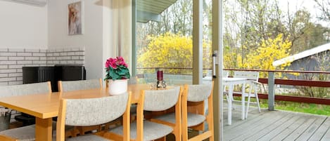 A dining area with a wooden table and chairs, a hanging light fixture, and a view of the outdoors.