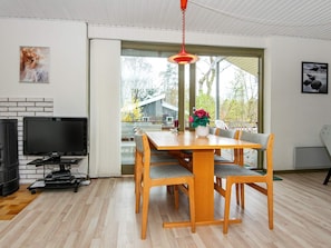 A modern living room with a wooden dining table, grey cushioned chairs, a flat-screen TV, and a red hanging light fixture. - 6 Person Holiday Home in Glesborg (Glesborg)