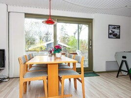 Ein Essbereich mit einem Holztisch und Stühlen, einer roten Hängeleuchte und Blick durch eine große Schiebeglastür.
