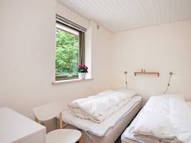 Un dormitorio con dos camas, una mesita, una ventana con vistas a la vegetación y una estantería con una lámpara.