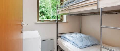 A bunk bed room with a window, a small cabinet, and a radiator.