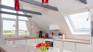 A compact kitchen with a dining area, featuring a table with a vase of red tulips, a coffee machine, and a view of the outdoors through a skylight. - 12 Person Holiday Home in Lemvig (Lemvig)