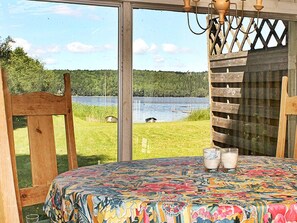 A room with a large window overlooking a lake, a table with a colorful tablecloth, and two glasses of a beverage.