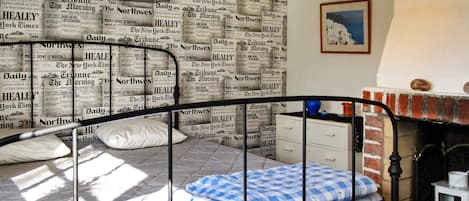 A bedroom with a bed, pillows, a dresser, a fireplace, and a framed picture on the wall.