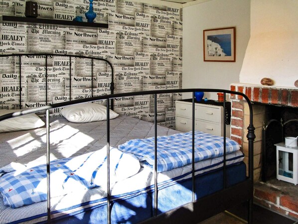 A bedroom with a bed, pillows, a dresser, a fireplace, and a framed picture on the wall.