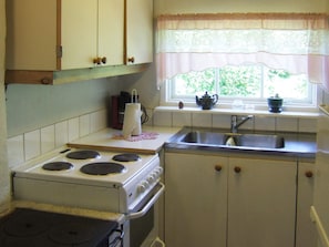 Une cuisine de taille réduite, équipée d’une cuisinière, d’un évier et d’une fenêtre avec des rideaux.