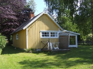 Un petit bâtiment en bois jaune, avec une fenêtre blanche et une porte en bois, entouré de verdure.