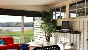 A room with a table, chairs, a red sofa, a TV, and a view of a lake. - 4 Person Holiday Home in Lerdala (Lerdala)