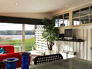 A room with a table, chairs, a red sofa, a TV, and a view of a lake. - 4 Person Holiday Home in Lerdala (Lerdala)